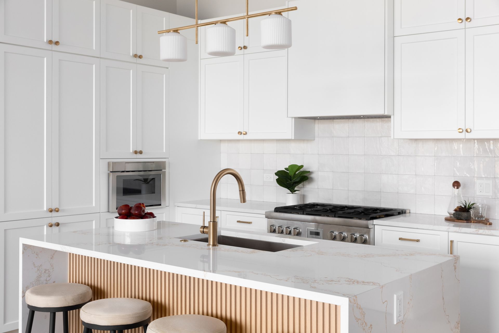 A kitchen with white cabinets , a stove , sink , and stools.