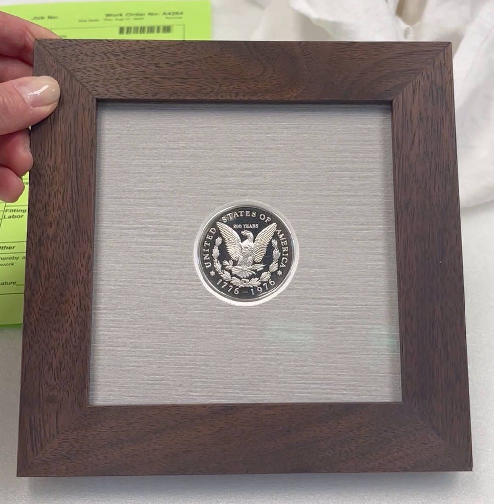 A person is holding a picture frame with a coin in it