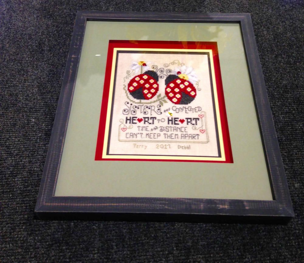 A framed cross stitch with ladybugs and the words