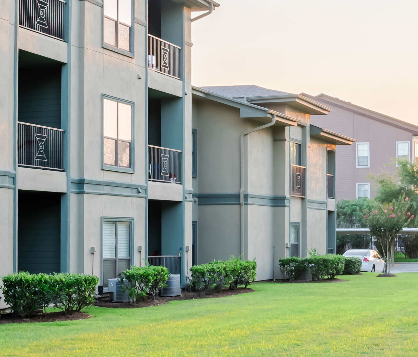 A row of apartment buildings with balconies and a lush green lawn in front of them