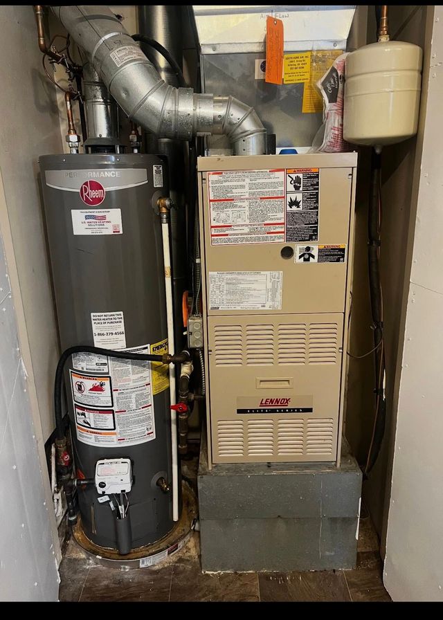 Water heater and furnace in a narrow utility closet with metal ductwork and pipes.
