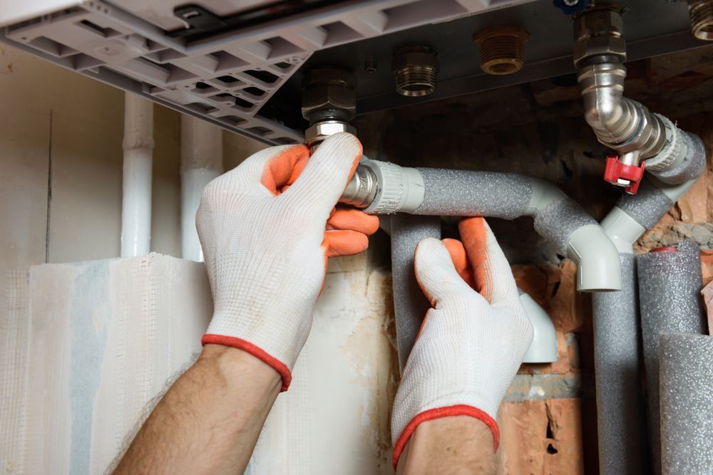 A man wearing gloves is fixing a pipe with a wrench.