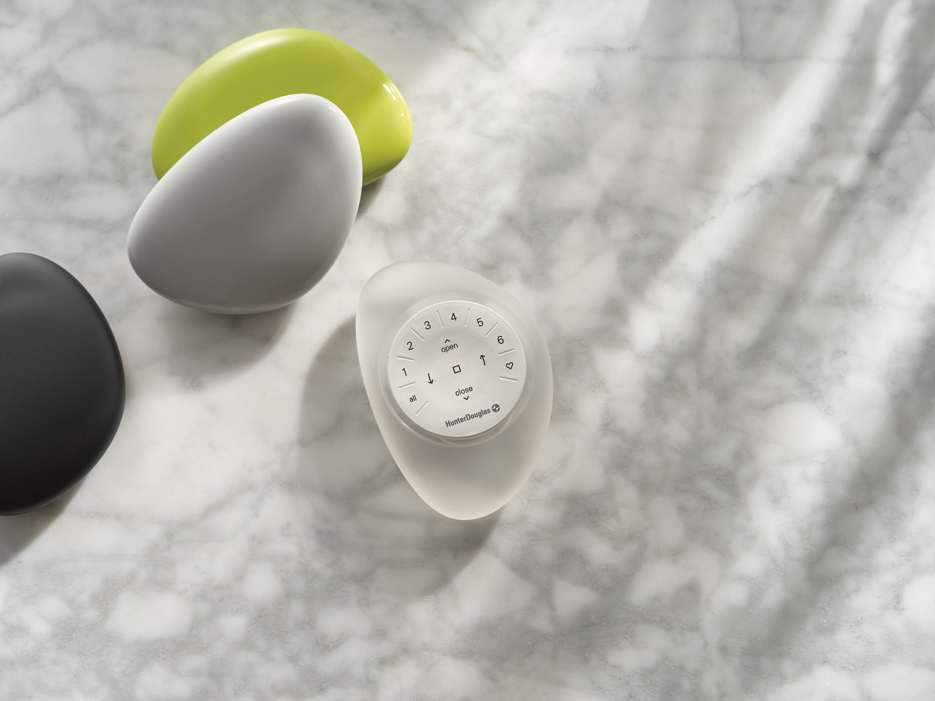 Four smooth, pebble-shaped objects in gray, lime, black, and translucent white rest on a light marble surface.