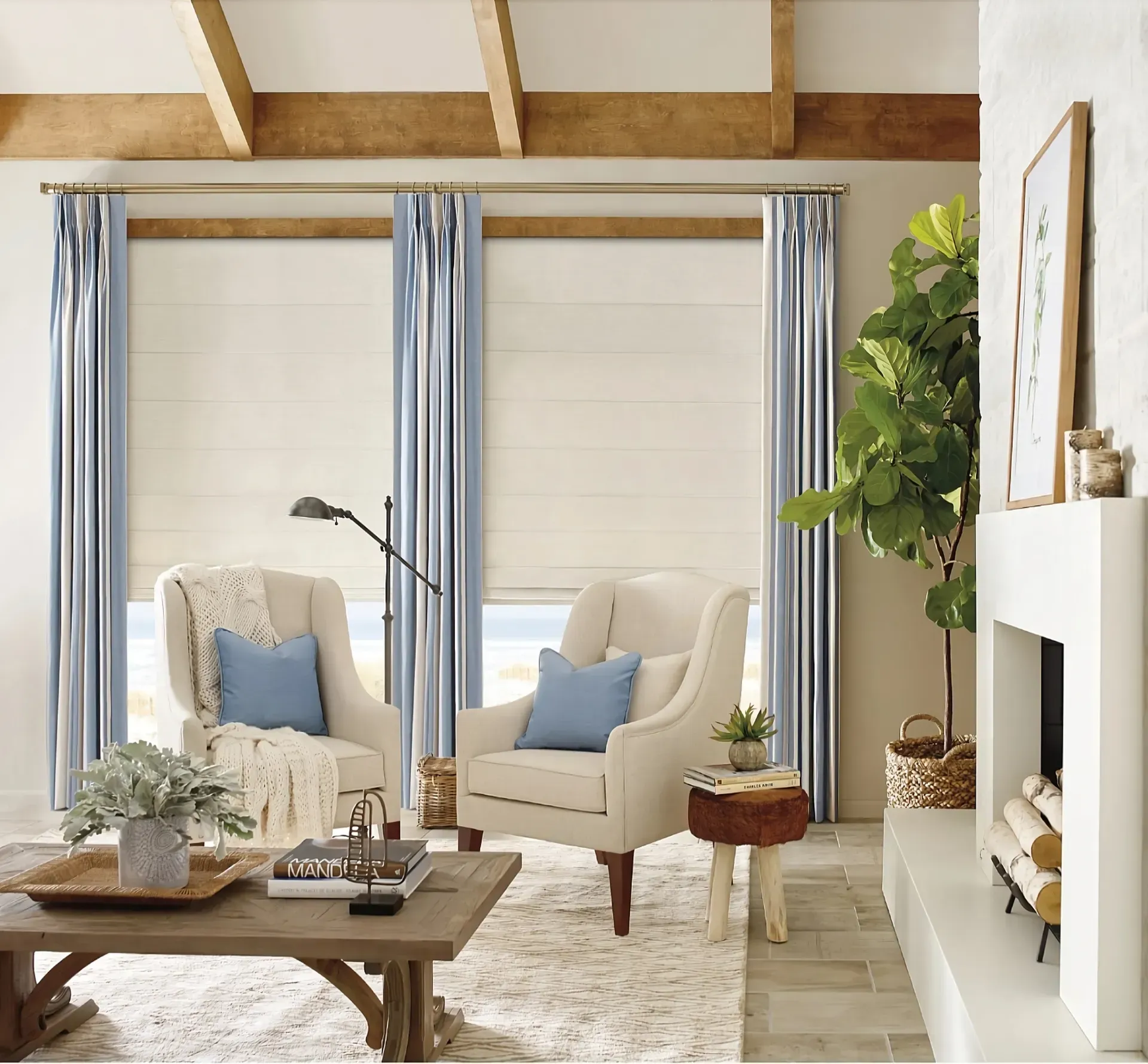 Two cream armchairs with blue pillows in a cozy living room with striped curtains, a wooden coffee table, and fireplace.