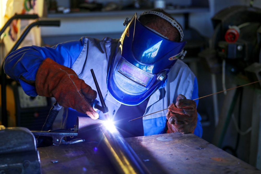 A Man Wearing A Welding Mask Is Welding A Metal Pipe — BM Steel Fabrication In Forster, NSW