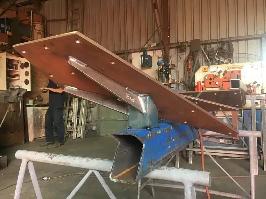 A Man Is Working On A Piece Of Metal In A Factory — BM Steel Fabrication In Forster, NSW