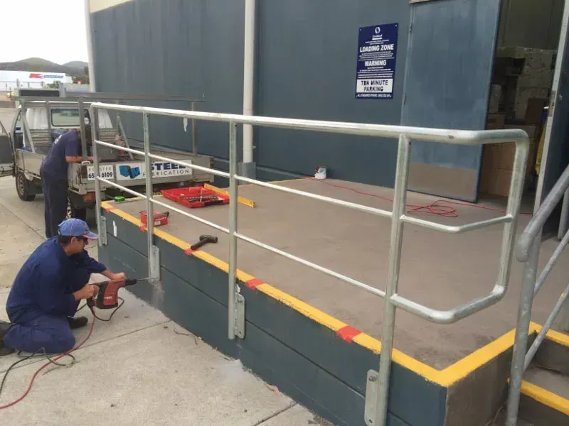 Two Men Are Working On A Railing Outside Of A Building — BM Steel Fabrication In Forster, NSW