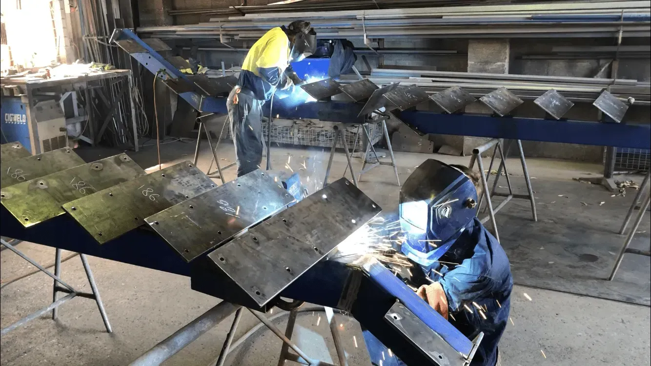A Man Is Welding A Metal Structure In A Factory — BM Steel Fabrication In Forster, NSW