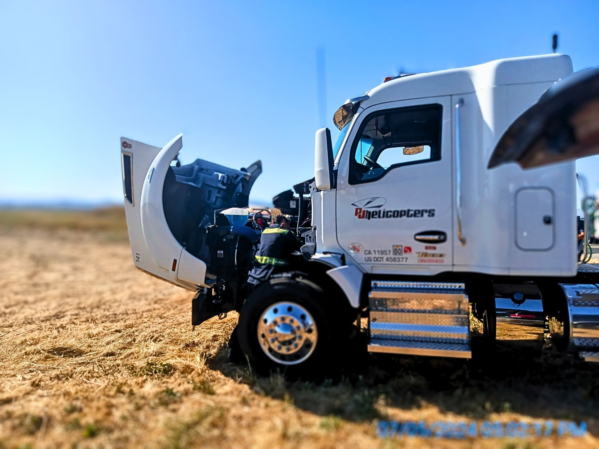 A white truck with the hood up is parked in a field.