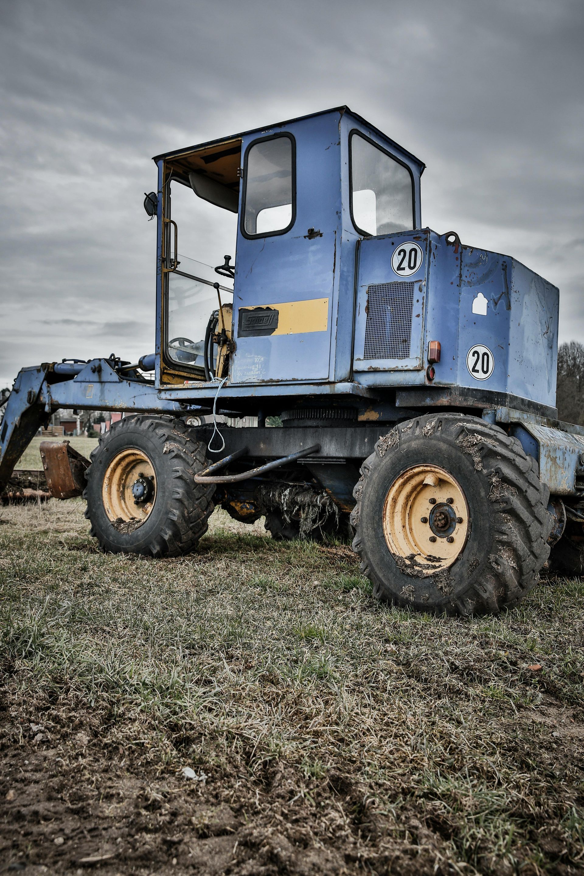 An old blue and yellow tractor is parked in a field.