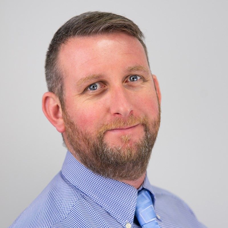 A man with a beard is wearing a blue shirt and tie.