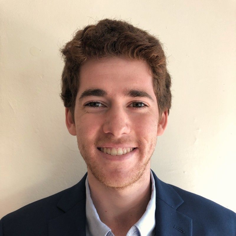 A young man in a suit and shirt is smiling for the camera.