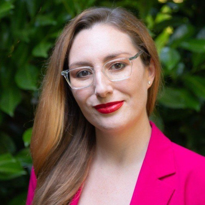 A woman wearing glasses and a pink jacket is posing for a picture.