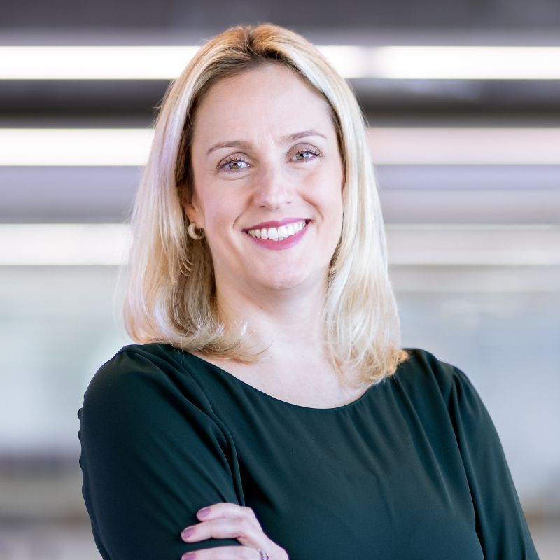 A woman in a black dress is smiling with her arms crossed.