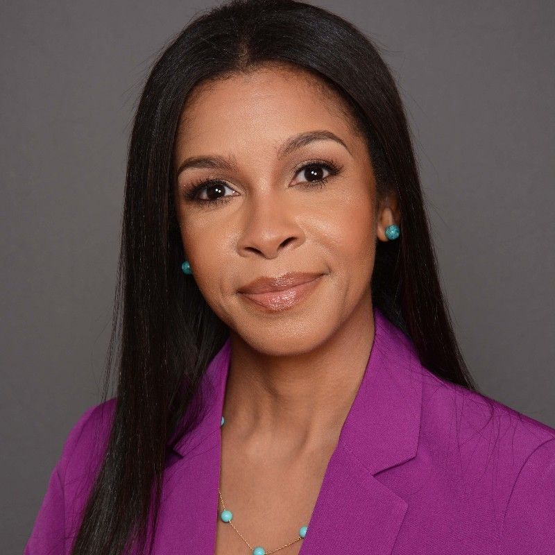 A woman wearing a purple jacket and a necklace is smiling for the camera.