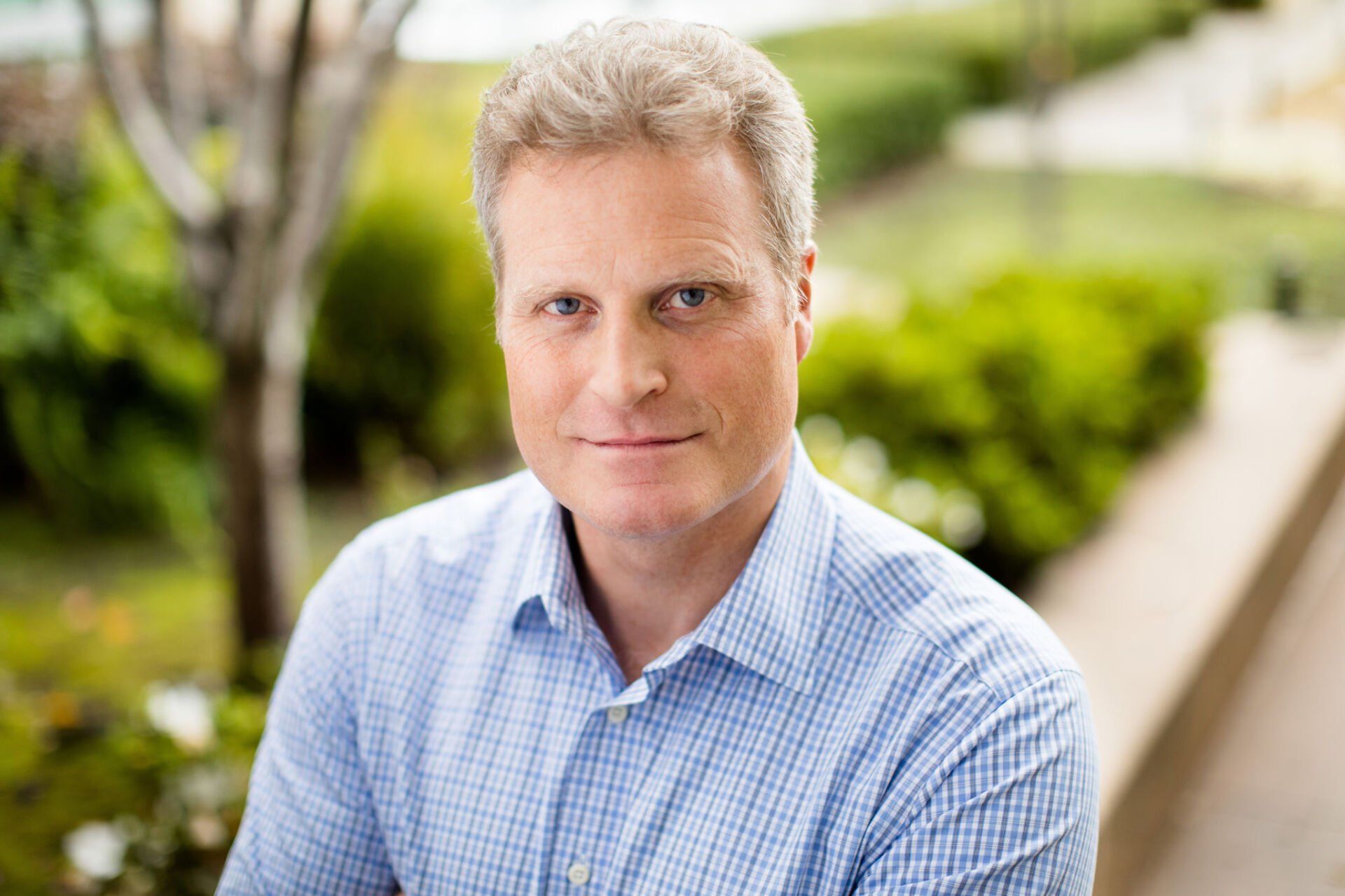 A man in a blue shirt is sitting outside and smiling for the camera.