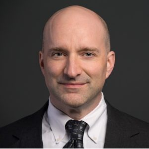 A bald man wearing a suit and tie smiles for the camera