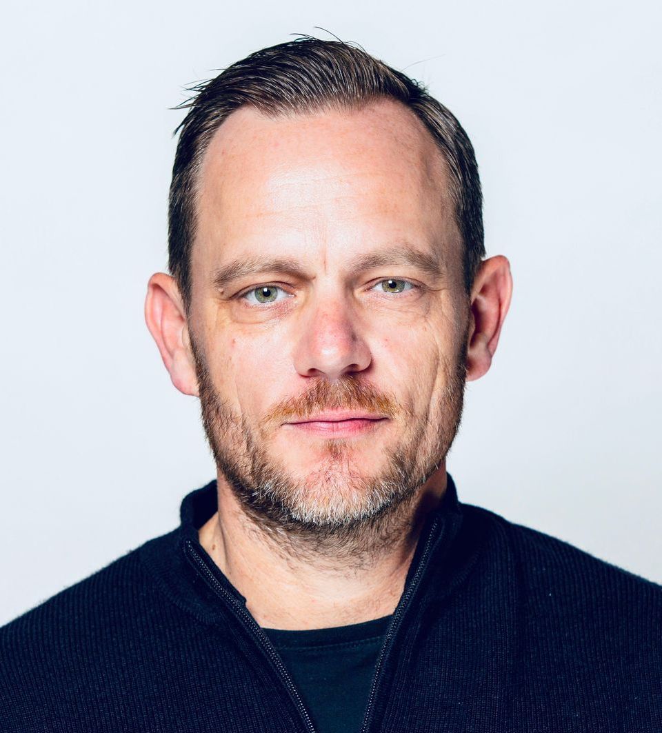 A man with a beard is wearing a black sweater and looking at the camera.