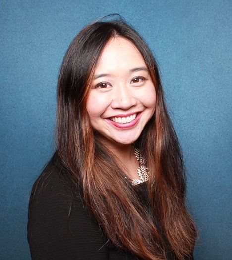 A woman with long hair is smiling in front of a blue background.