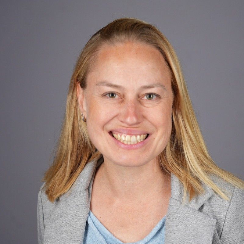A woman wearing a gray jacket and a blue shirt is smiling for the camera.
