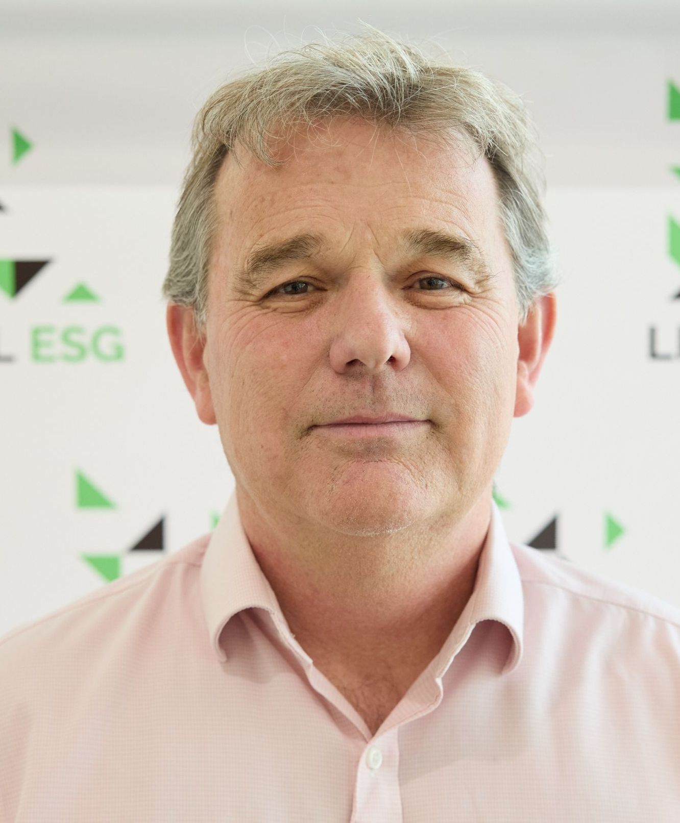 A man in a pink shirt is smiling in front of a sign that says esg