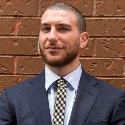 A man in a suit and tie is standing in front of a brick wall.