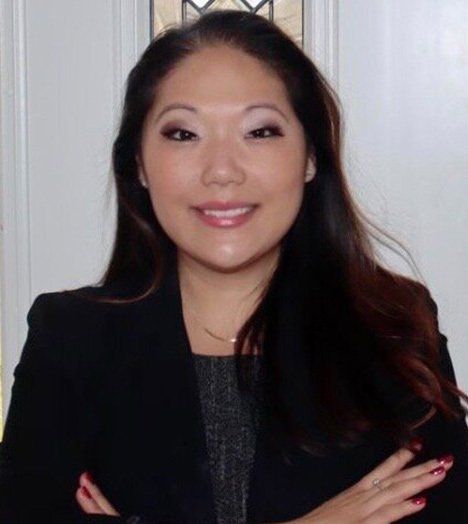 A woman in a black jacket is smiling with her arms crossed