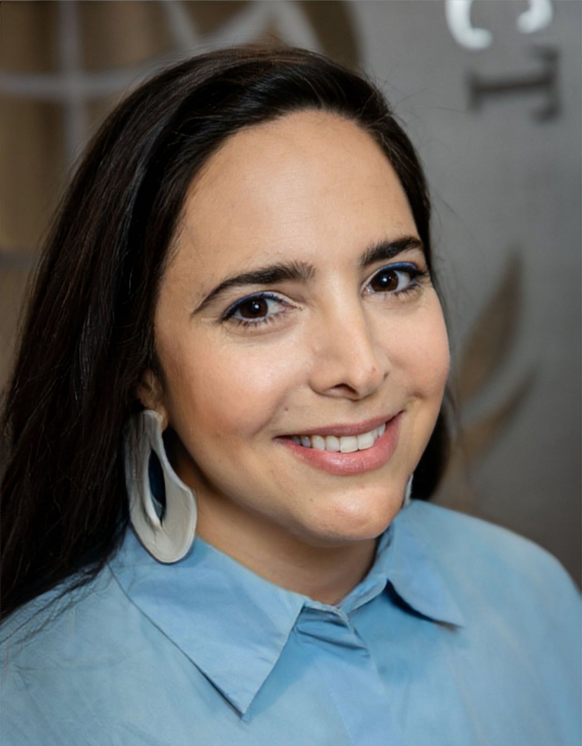 A woman wearing a blue shirt and earrings is smiling for the camera.