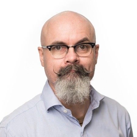 A bald man with a beard and mustache wearing glasses and a blue shirt.