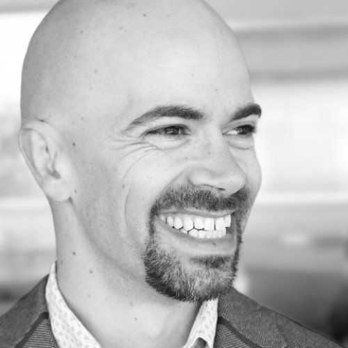 A bald man with a beard is smiling in a black and white photo
