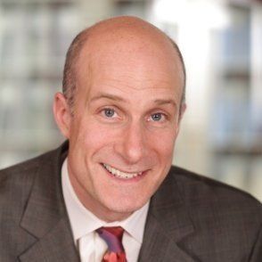 A bald man in a suit and tie smiles for the camera