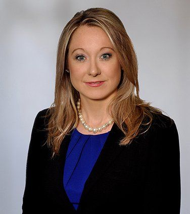 A woman wearing a black jacket and a blue shirt is smiling for the camera.