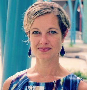 A woman wearing a blue dress and earrings smiles for the camera