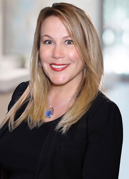 A woman wearing a black shirt and a blue necklace is smiling for the camera.