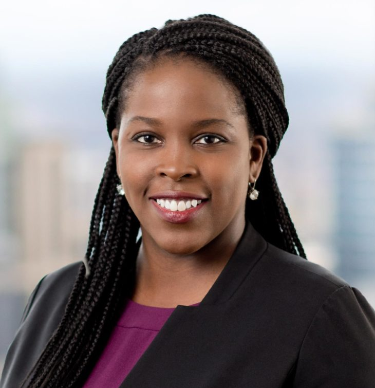 A woman with braids is smiling and wearing a black jacket