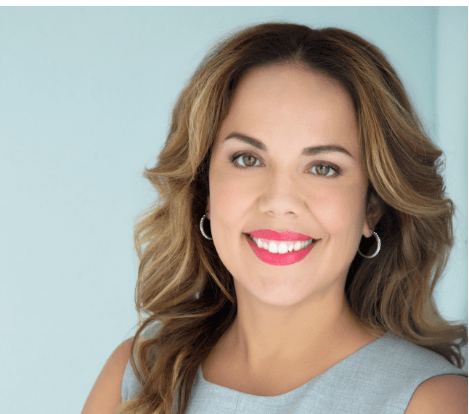 A woman with long hair and hoop earrings smiles for the camera