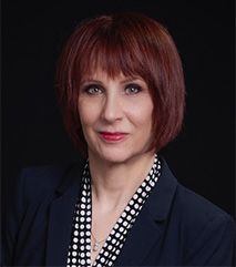 A woman with red hair is wearing a blue jacket and a polka dot shirt.