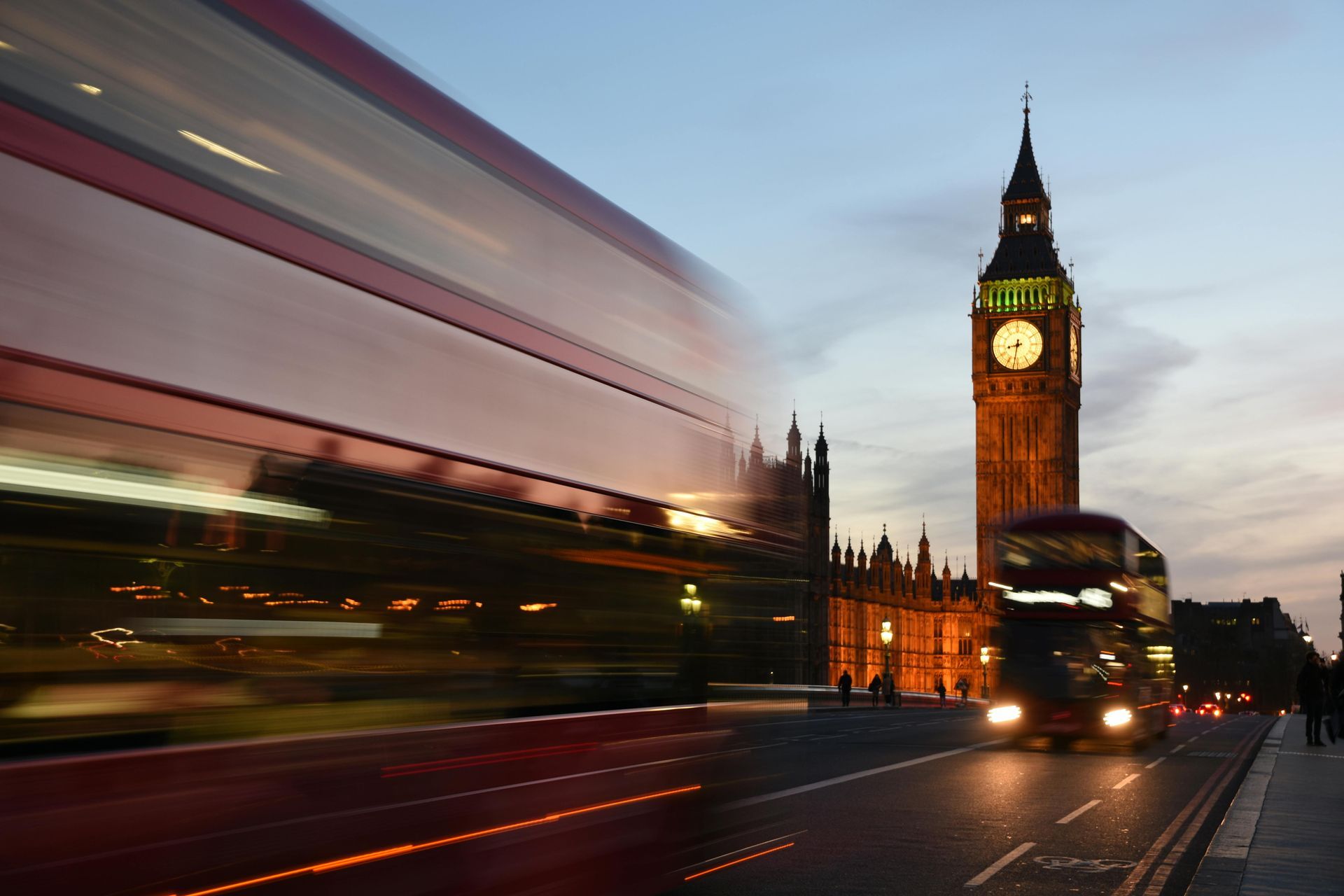 A double decker bus is driving down a street in front of big ben clock tower.