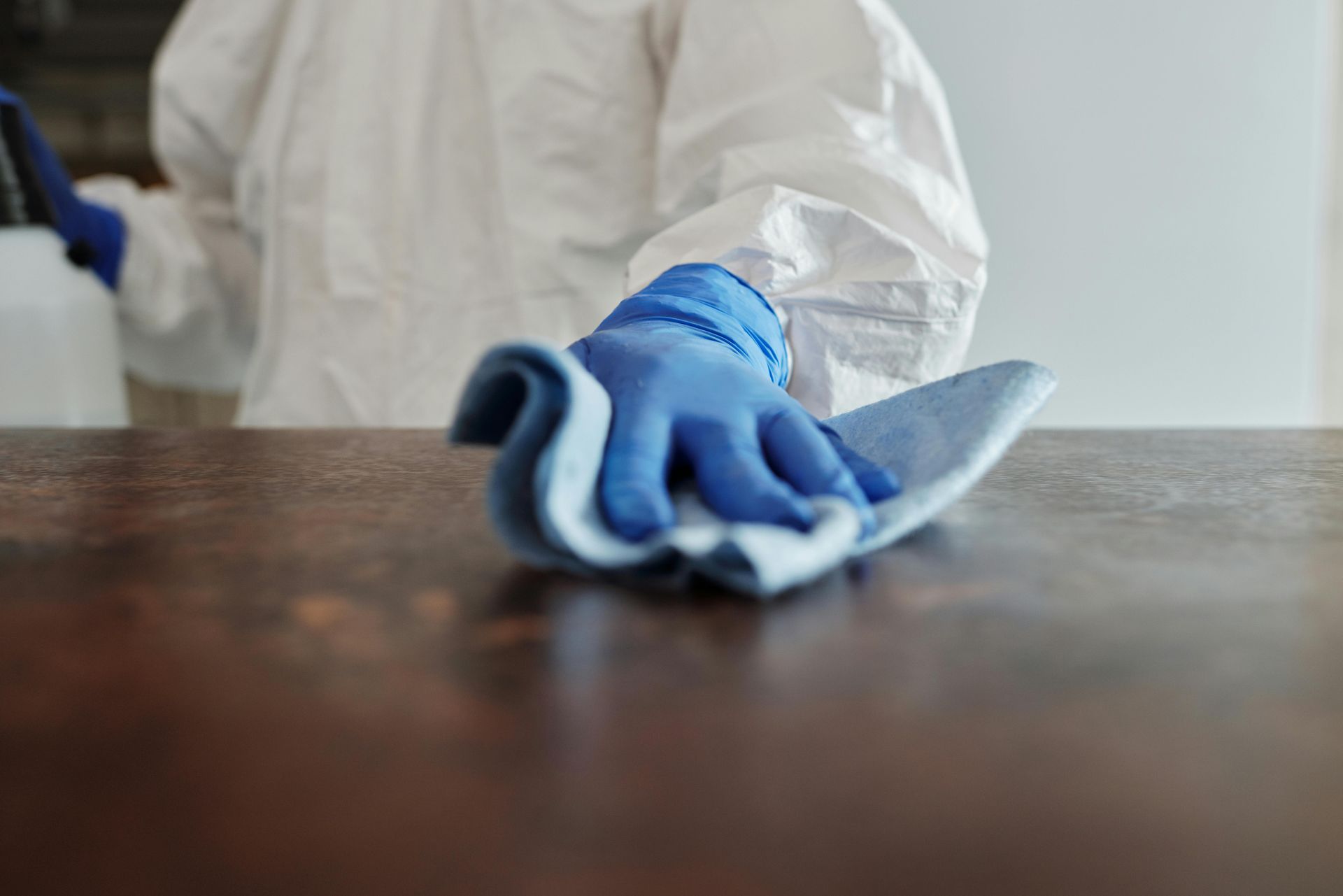 Person in hazmat suit and blue gloves wiping a brown surface with a blue cloth.