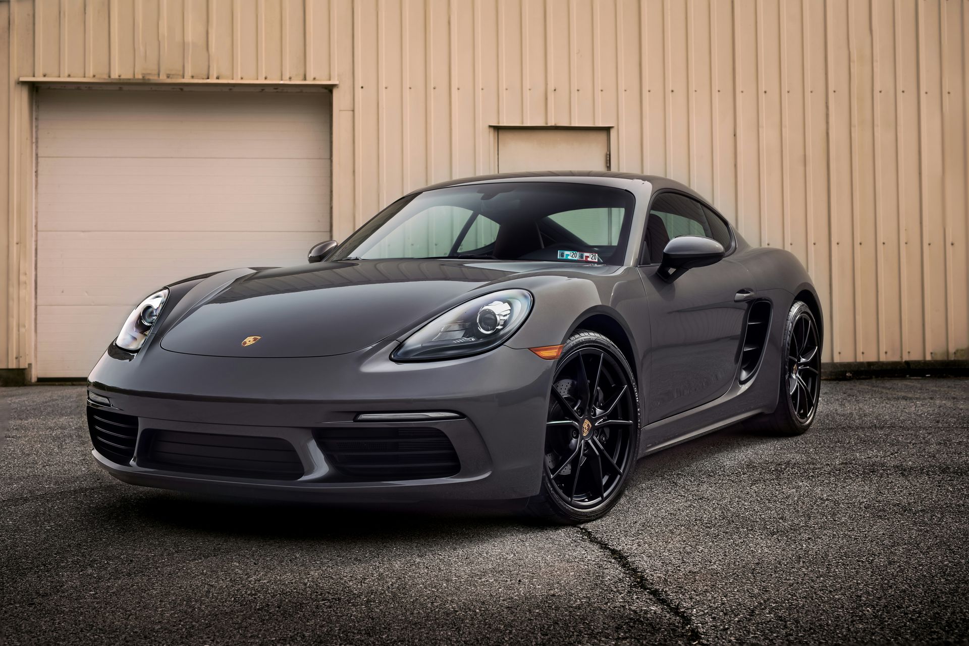 A gray porsche boxster is parked in front of a garage door.