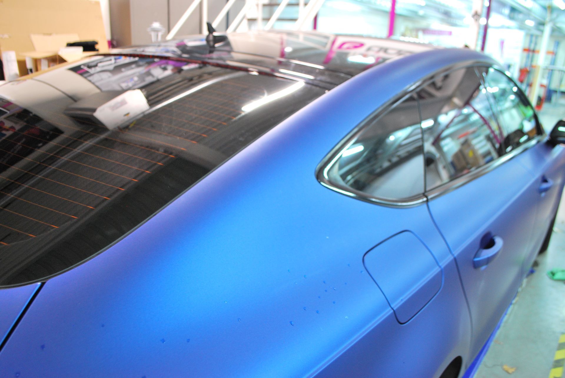 A blue car with a black roof is parked in a garage.