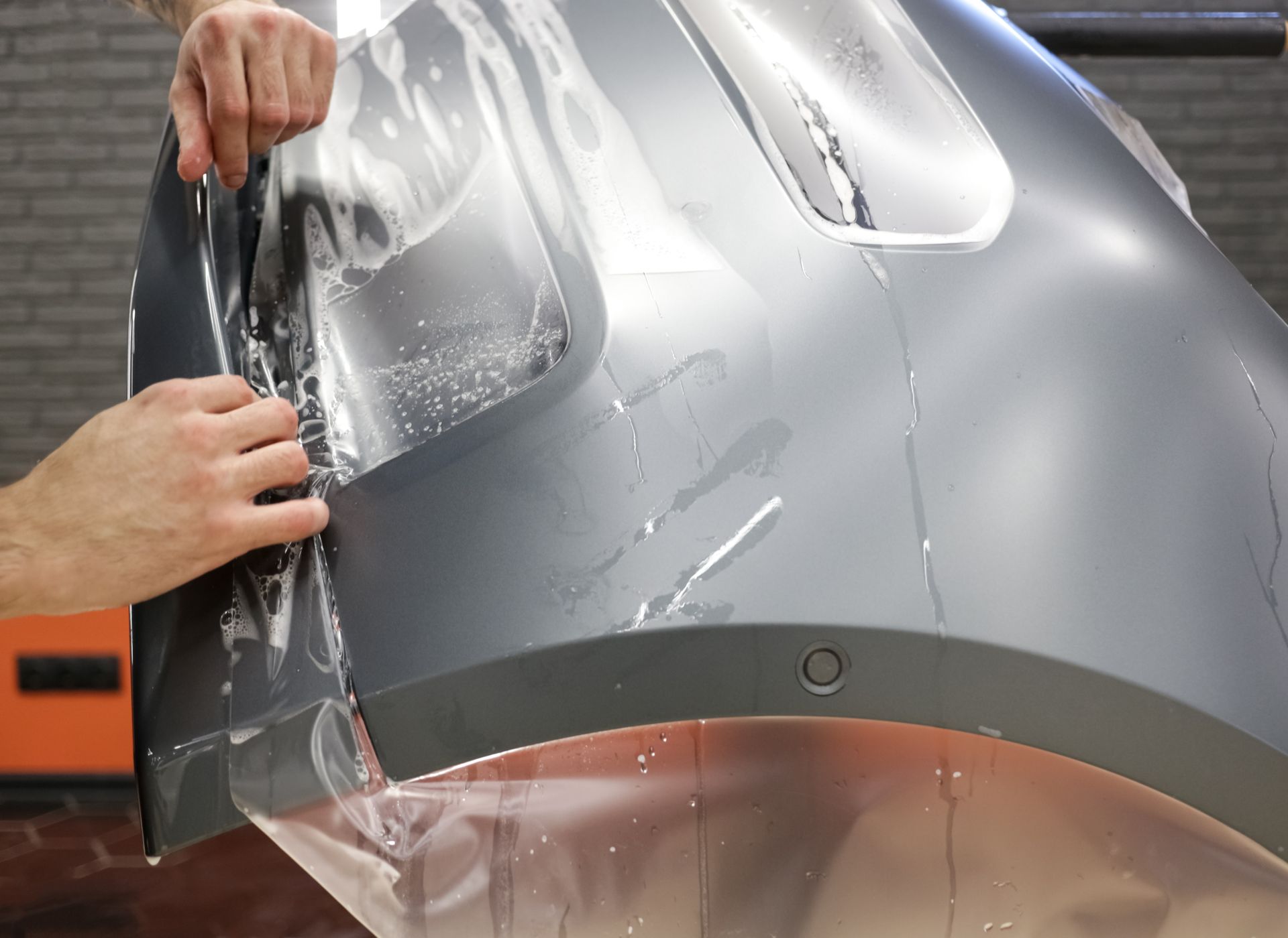 A person is applying a protective film to a car bumper.