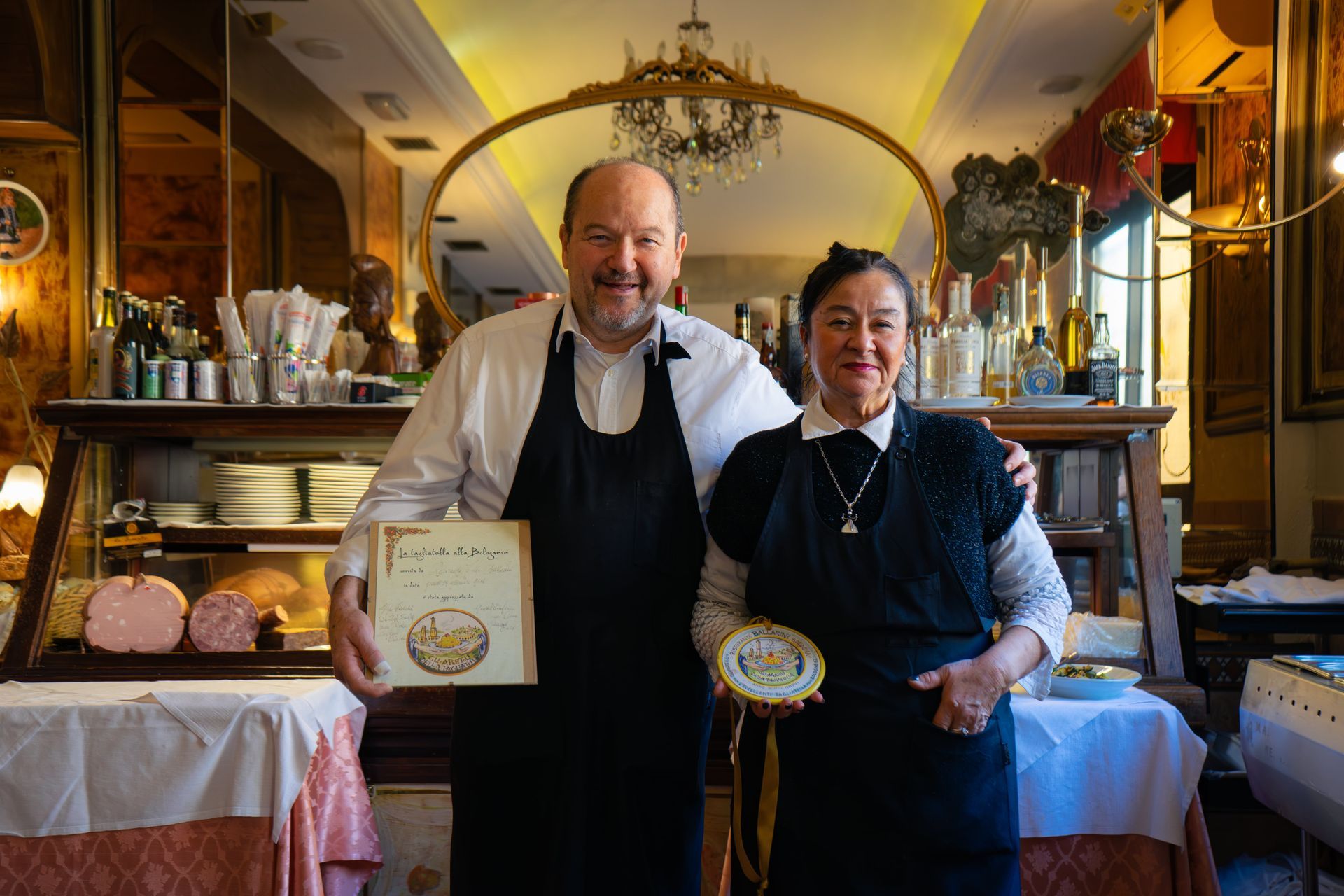 Due persone in grembiule posano in un ristorante, tenendo in mano dei premi.
