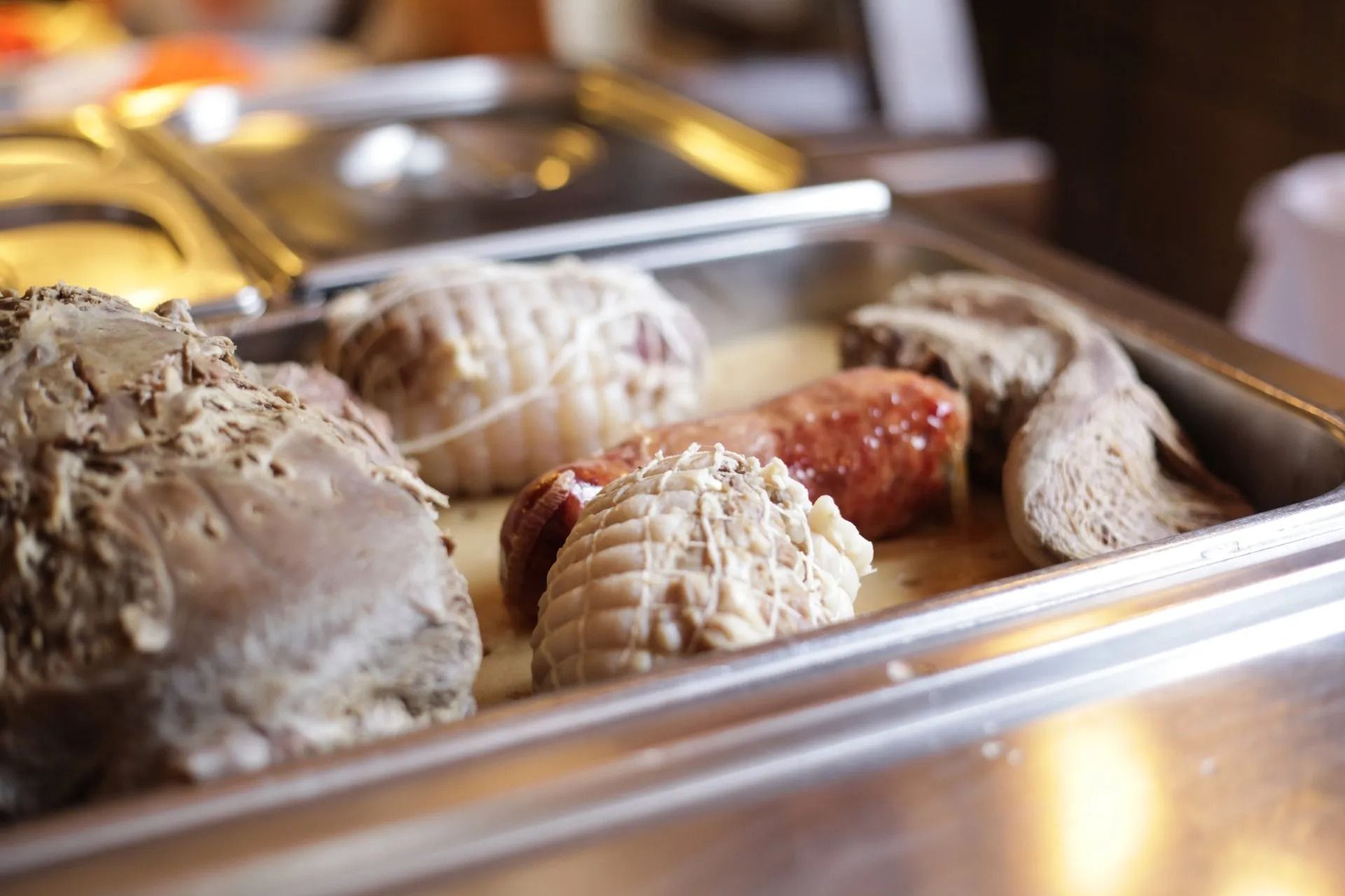 Il vassoio di metallo contiene carni cotte: salsicce, tagli arrotolati e un grosso pezzo di carne, possibilmente la lingua.