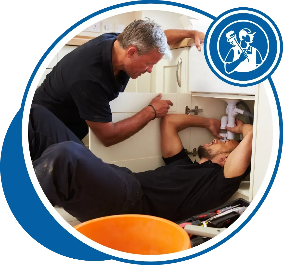 Two plumbers working under a sink, one helping the other.