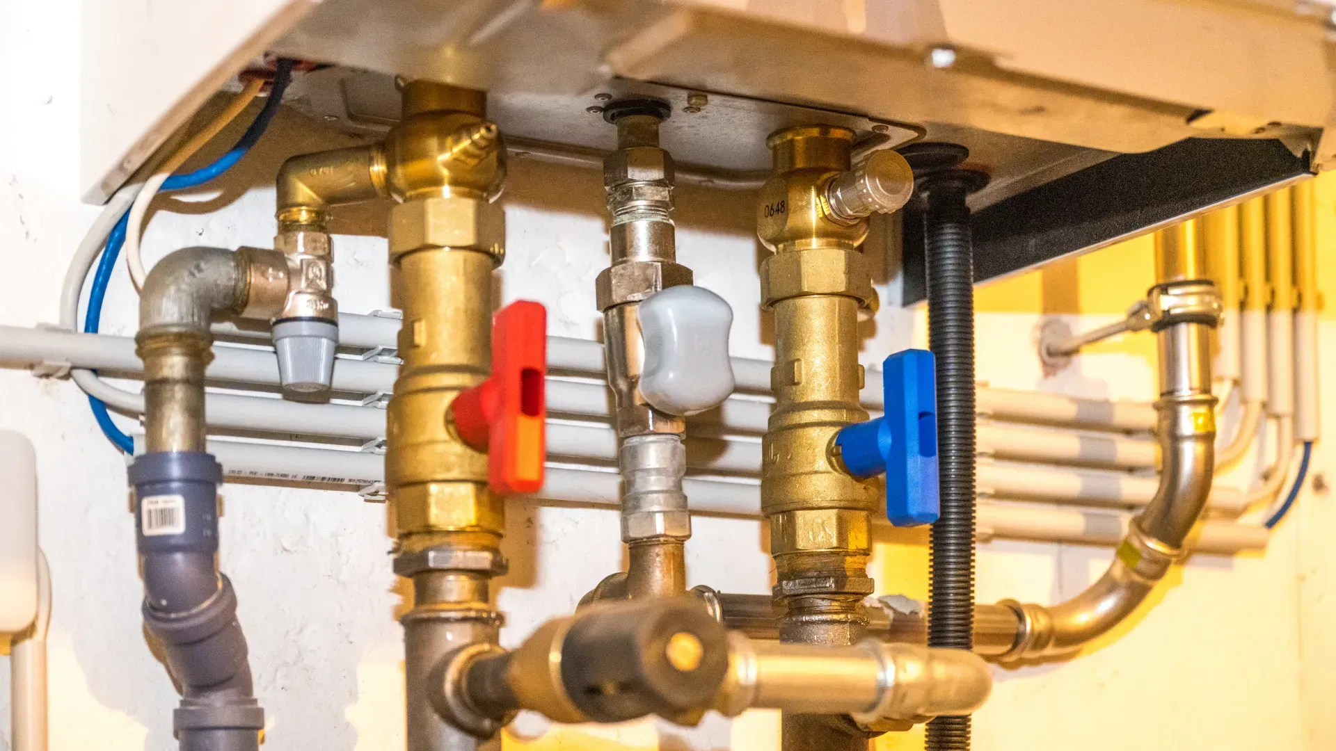 Close-up of pipes with red, gray, and blue valves attached to a boiler.