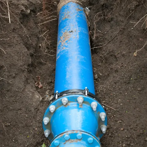 Blue water pipe section in an open trench, bolted and ready for installation.