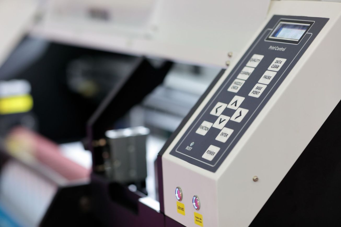 A man is holding a piece of paper in front of a printing machine.