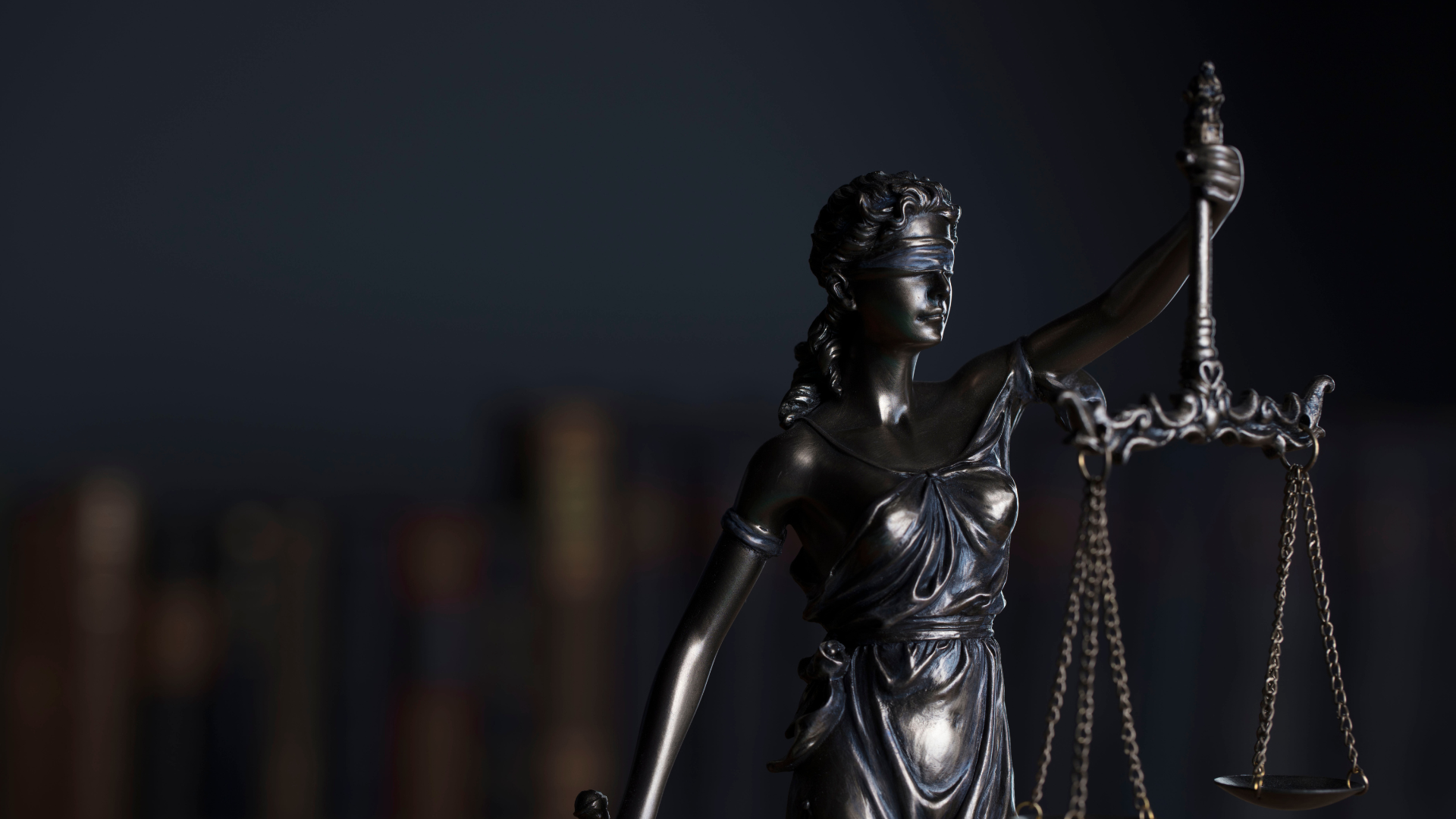 Statue of Lady Justice holding scales and sword, blindfolded, dark background.