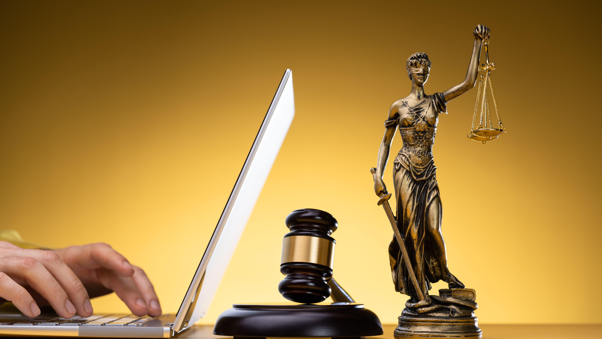 Person using laptop next to a gavel and Lady Justice statue. Golden background.